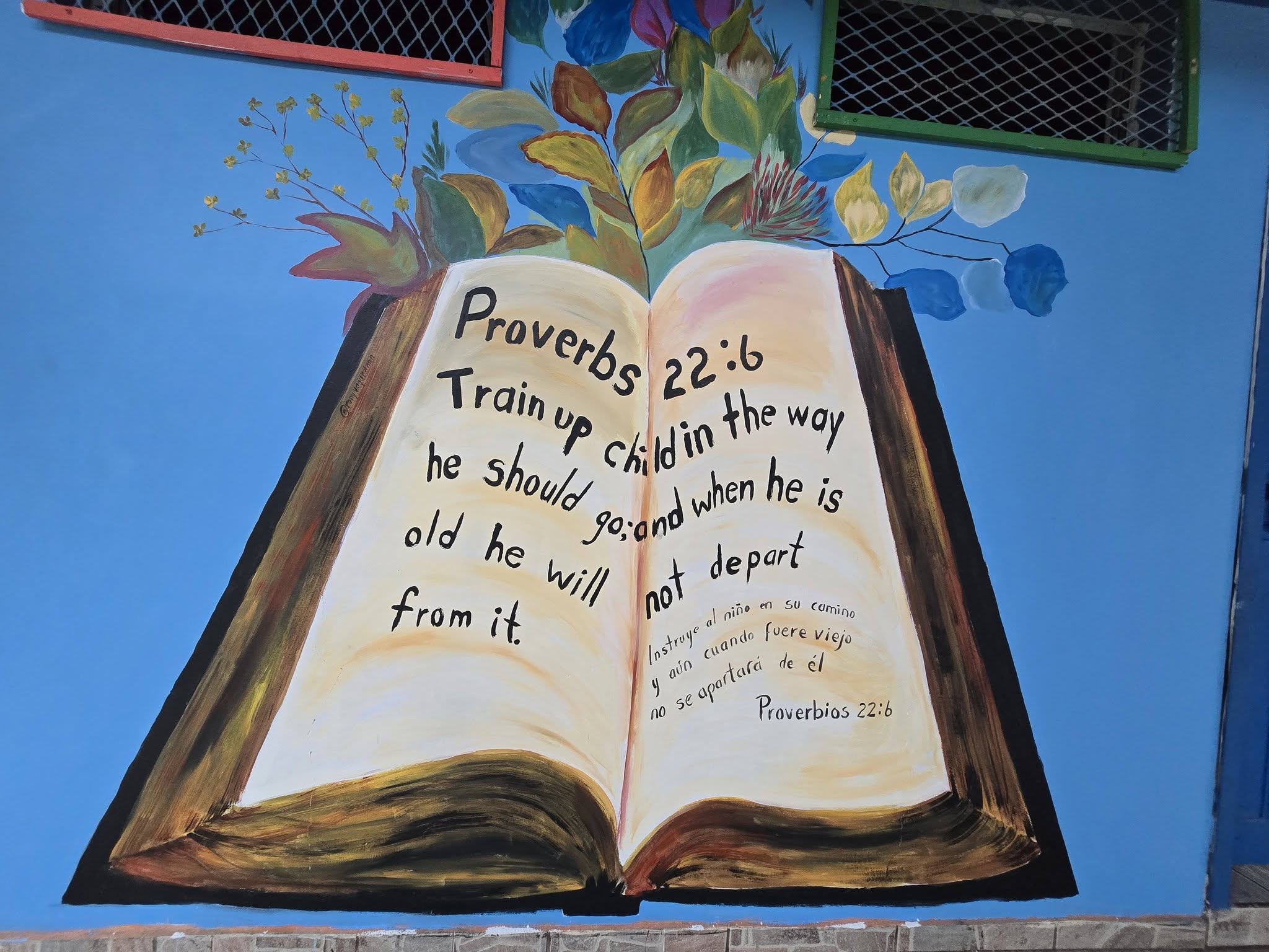 Mural del colegio con el pasaje de Proverbios 22:6 pintado sobre un libro abierto